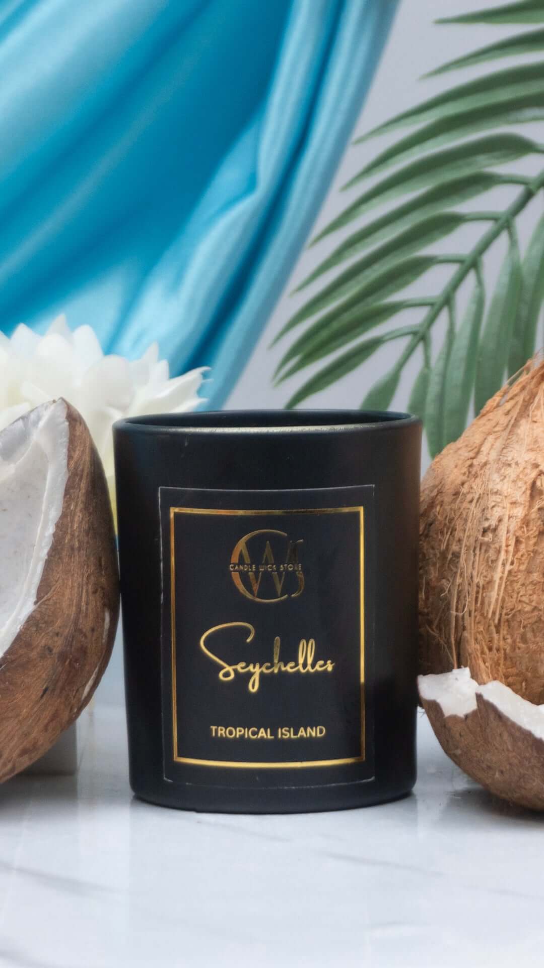 Seychelles scented candle in black jar surrounded by coconuts, evoking tropical island atmosphere.
