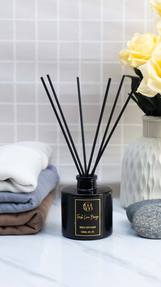 Fresh Linen Breeze Reed Diffuser with black reeds beside stacked towels and flowers, creating a clean ambiance.